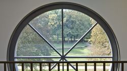 Kulaté okno se zkříženými vzpěrami. Z okna se otvírá pohled do jarního parku.