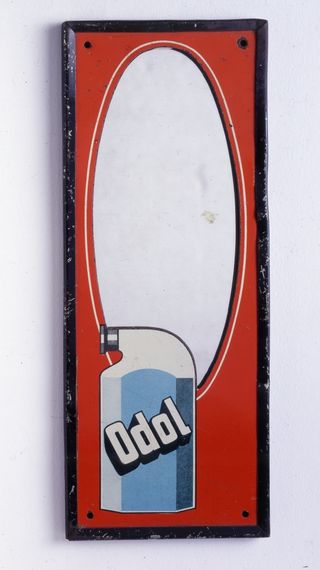 Ein alter Spiegel mit roter Fläche und einer Odol-Flasche links unten.