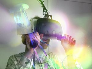 Eine junge Frau blickt durch eine Virtual-Reality-Brille. Sie ist umgeben von bunten Lichtspots, die das Innere eines Aquariums simulieren. Schemenhaft sind Quallen zu erkennen.