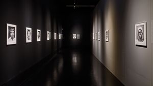 Ein Ausstellungsraum mit schwarzen Wänden. An den Wänden hängen vier beleuchtete schwarz-weiß Porträts. 