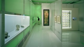 Ein hellgrüner Ausstellungsraum. Auf der linken Seite eine Vitrine, in der ein Schädel, eine Kartee und ein gläserner Kopf stehen. Auf der linken Seite, in einer beleuchteten Vitrine, MRT-Aufnahmen eines Gehirns.