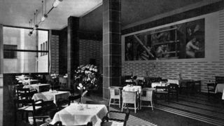 Schwarz-weiß-Aufnahme der Museumsgaststätte mit leeren Stühlen und Tischen. Im Hintergrund das Wandgemälde von Otto Dix.