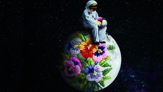 Ein Astronaut sitzt auf der Weltkugel, die von gestrickten Blumen umrankt ist. In seinen Händen hält er Wollknäuel und Stricknadeln. Im Hintergrund das All.