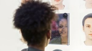 Eine junge Frau schaut in einen Spiegel an einer Station zum Thema Schönheitsideale. Links und rechts des Spiegels befinden sich Bilder unterschiedlicher Gesichter.