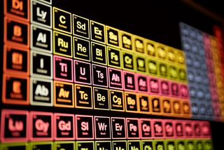Eine chemische Periodentafel in bunten Farben auf schwarzem Hintergrund. Statt der Namen der chemischen Elemente steht unter den Kürzeln eine Emotion, z.B. &quot;U Uneasy&quot; (statt &quot;Uran&quot;).
