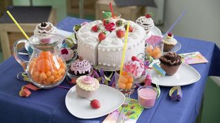 Auf einem Tisch mit blauer Tischdecke stehen verschieden Kuchen und Torten, Obst und Getränke.