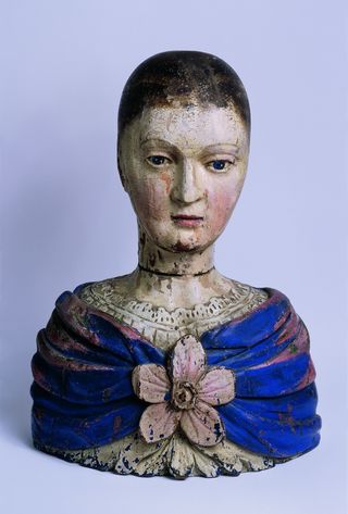 Weiblicher Perückenkopf von 1700. Auf ihrem Oberteil hat die weibliche Figur einen blauen Schal mit einer rosa Blume.