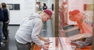 Ein Jugendlicher mit grauem Kapuzenpullover und rotem Basecap löst in der Dauerausstellung eine Aufgabe .