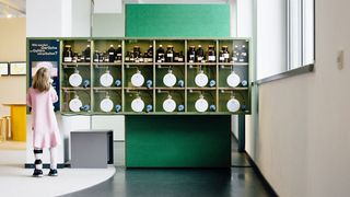 Ein Mädchen steht vor einer Wand, in der Apothekergläser stehen.