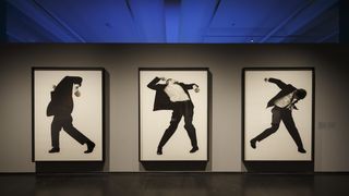 An einer grauen Wand drei lebensgroße schwarz-weiß Bilder. Auf den Bildern jeweils ein Mann in Tanz-Posen. Er trägt einen schwarzen Anzug und ein weißes Hemd.