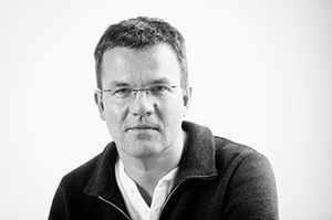 Schwarzweißes Porträt von Jörg Gläscher, der nach vorne guckt und eine Jacke trägt.