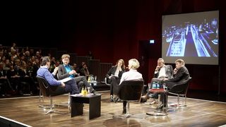 Auf einem Podium sitzen Frauen und Männer im Kreis und unterhalten. Rechts im Hintergrund sitzt Publikum.