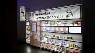 In einer beleuchteten Vitriene befinden sich mehrere Exponate. In dem obersten Regal der Vitriene befindet sich ein Banner mit der Aufschrift: &quot;Im Gedenken an Marwa El-Sherbini&quot;