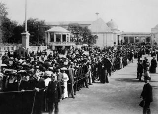 Ein schwarzweißes Foto der I. Internationalen Hygiene-Ausstellung 1911. Viele Menschen stehen in einer breiten Schlange um zur Halle &quot;Der Mensch&quot; zu gelangen. Der Andrang wird durch Absperrungen und Polizeibeamte geregelt.