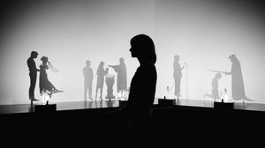 Im Hintergrund ein Schattentheater, das mit animierten Silhouetten Sprachrituale wie beispiesweise bei der Hochzeit oder Taufe nachstellt. Im Vordergrund eine junge Besucherin, die verschattet ist.