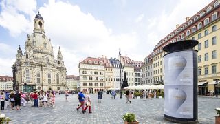Litfassäule mit einem Ausstellungsplakat auf dem Dresdner Neumarkt,  im Hintergund Touristen und die Frauenkirche