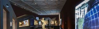 Die Ausstellung Scham mit der Statue des nackten griechischen Dichters Anakreon im Zentrum des Bildes. Im Vordergrund rechts eine farbige Videoprojektion. Links und im Hintergrund Exponate zum Thema Scham.