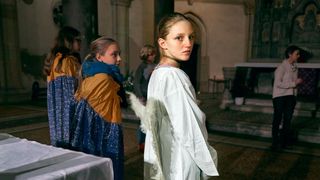 Im Zentrum des Fotos ist eine junge Engelsdarstellerin beim Krippenspiel, ihr Kopf ist nach hinten gedreht und sie schaut in die Kamera. Links von ihr stehen zwei verkleidete Mädchen.