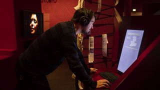 Ein Besucher mit Kopfhörern in einem roten Raum vor einer Medienstation mit Computer und Tastatur.