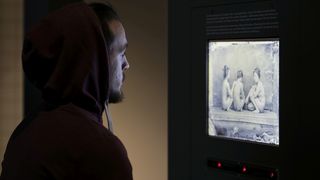 Ein junger Mann bertachtet einen Monitor, der ein schwarzweißes historisches Foto von drei Frauen aus Asien zeigt.