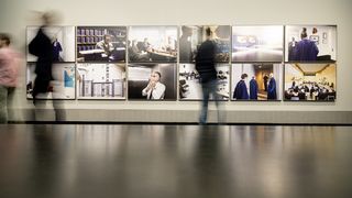 Besucher vor einer weißen Wand mit großformatigen Fotografien. Die Bilder dokumentieren den Arbeitsalltag am Internationalen Strafgerichtshof von Den Haag.