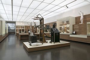 Der Ausstellungsraum Gläserner Mensch in der Dauerausstellung. Die Wände sind weiß, die Vitrinenwände aus braunem Holz. In der Mitte des Raums steht die Gläserne Frau. Im Vordergrund und an den Wänden befinden sich Exponate, die die Geschichte der Erforschung des menschlichen Körpers veranschaulichen.