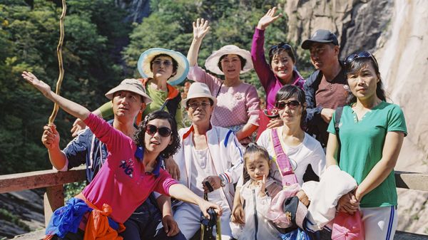 Eine koreanische Wandergruppe posiert vor einer bewaldeten Felswand für ein Gruppenfoto.