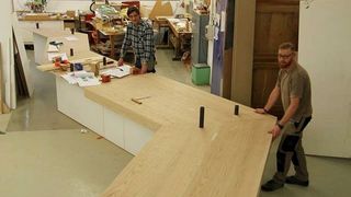 Zwei Werkstattmitarbeiter zeigen ein mäanderndes Ausstellungsmodul in Höhe eines Tisches