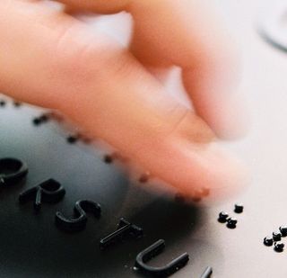Eine Hand tastet auf einem Schild mit Brailleschrift