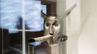 Eine metallene Schandmaske mit einer darauf geklebten metallenen Flöte aus dem 17. Jahrhundert in einer Vitrine.