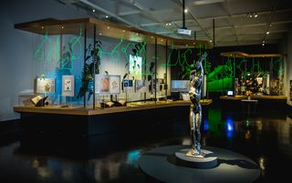 Der erste Raum der Pflanzenausstellung. Im Vordergrung steht eine Statue. Im Hintergrund andere Objekte und neon-grüne Schrift.