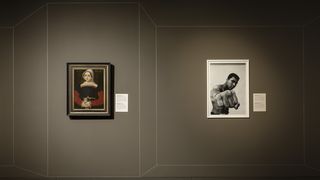 Ein Gemälde und eine Fotografie an einer hellbraunen Wand. Das linke Gemälde ein antikes Ölgemälde mit der Porträtaufnahme einer Frau, die ihre Hände faltet. Die rechte Fotografie eine Porträtaufnahme von Muhammad Ali, der seine geballte Faust der Kamera entgegenstreckt.