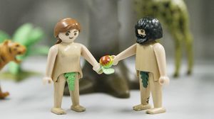 Nahaufnahme von zwei Playmobilfiguren als Adam und Eva im Paradies mit Apfel und feigenblattbedeckter Scham.