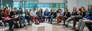 Ein Gesprächsrunde sitzt halkreisförmig in einem Saal. In der Mitte steht ein kleiner Tisch.