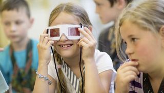 Zwei Jungen im Hintergrund und zwei Mädchen im Vordergrund im Kinder-Museum. Eins der Mädchen trägt eine 3D-Brille.