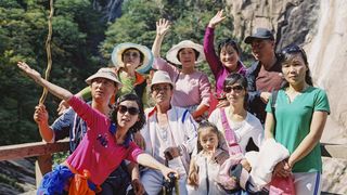 Eine koreanische Wandergruppe posiert vor einer bewaldeten Felswand für ein Gruppenfoto.