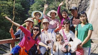 Eine koreanische Wandergruppe posiert vor einer bewaldeten Felswand für ein Gruppenfoto.