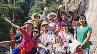 Eine koreanische Wandergruppe posiert vor einer bewaldeten Felswand für ein Gruppenfoto.