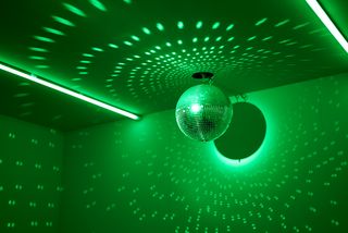 In einem grün ausgeleuchteten Raum wirft eine Diskokugel helle lichtreflexe an die Decke und die Wände.