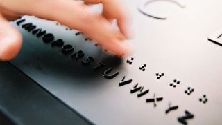 Ein Finger fährt über eine mit Brailleschrift versehene Beschriftung
