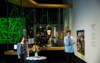 Ein Mädchen und ein Junge stehen in der Pflanzenausstellung. In der Mitte eine Vase mit einem Blumenstrauß auf einem Tisch.