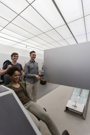 Eine junge Frau und zwei junge Männer an einer Mitmachstation im Raum Bewegung. Rechts im Hintergrund eine Balancierstrecke.