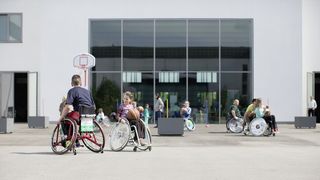 Einige junge Menschen spielen Rollstuhlbasketball auf dem Innenhof des Museums.