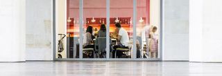Aufnahme des Museumsrestaurants aus der Froschperspektive. Leute sitzen um einen Tisch und essen. Im Hintergrund die Bartheke und Regale mit Flaschen und Gläsern.
