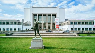 Die 4 Meter hohe Skultpur des Ballwerfers unter strahlend blauem Himmel mit dem Museumsgebäude im Hintergrund.  