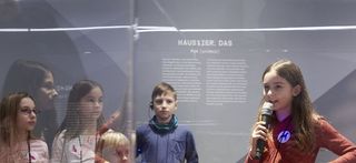 Ein dunkelhaariges Mädchen führt andere Kinder durch die Haustier-Ausstellung.