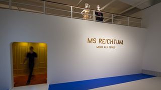 Eingang zum inszenierten Luxus-Schiff MS Reichtum, das die Kulisse der Ausstellung bildete. Auf dem Schiff stehen eine weibliche und eine männliche Schaufensterpuppe mit schicker Kleidung und Sonnenbrillen.