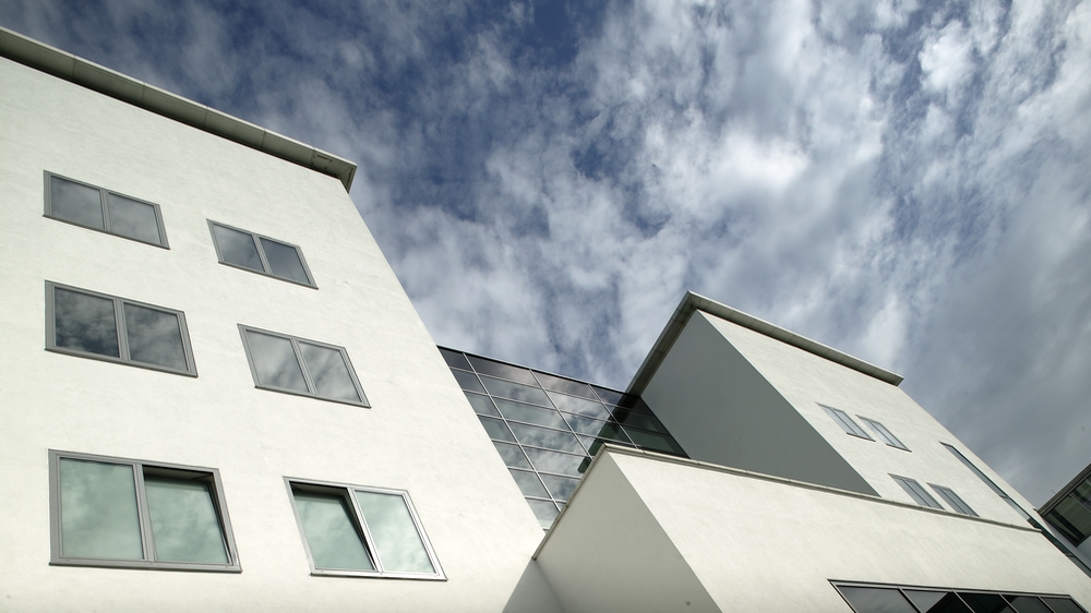 Rückansicht des Hauptgebäudes vom Innhof. Blick an der Fassade entlang in Richtung des leicht bewölkten Himmels.