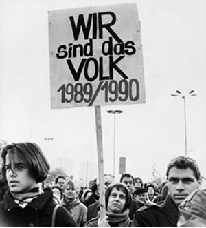Schwarzweißes Foto von Demonstranten, die im Jahr 1989 auf dem Berliner Alexanderplatz ein Schild mit der Aufschrift "Wir sind das Volk" zeigen.